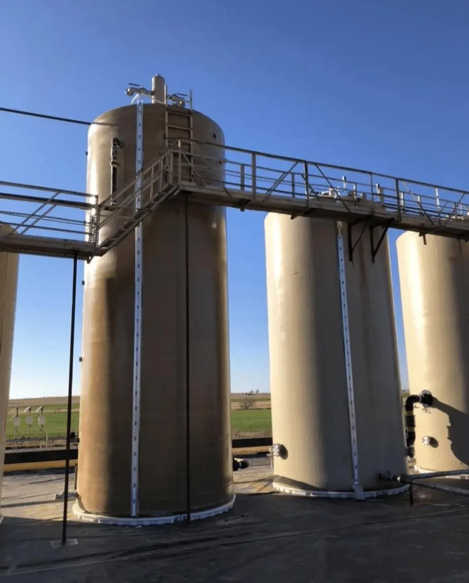 Tall beige vertical tanks with external water tank sight glass level indicators and metal stairways, designed for efficient liquid monitoring in industrial and agricultural sectors. The tanks ensure accurate inventory control for large-scale operations.