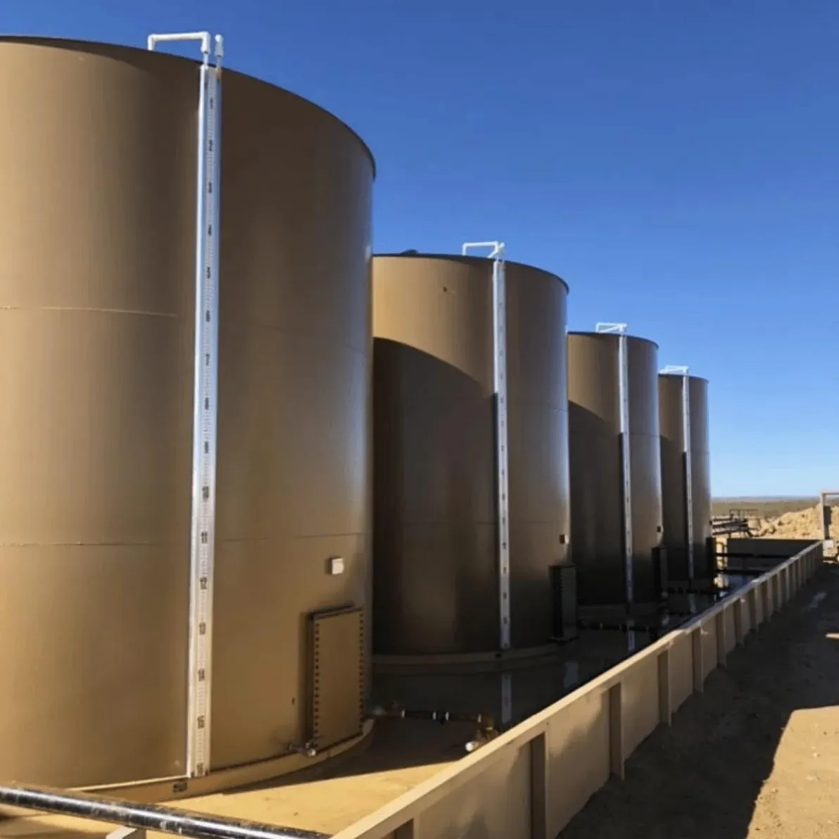 A row of beige industrial storage tanks with integrated tank sight glass level indicators for accurate liquid monitoring. Commonly used for oil, water, or chemical storage, these tanks highlight the importance of tank level sight glass systems in ensuring operational accuracy.