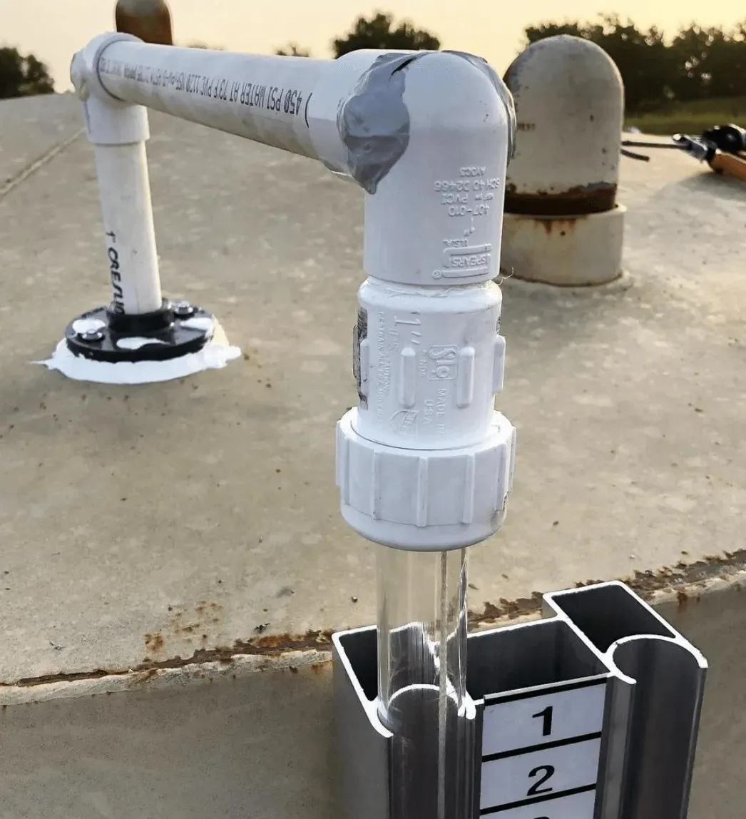 A close-up of sealed plumbing on a concrete tank top, designed to prevent vapor loss and maintain system efficiency. The setup includes a liquid level gauge for precise fluid monitoring.