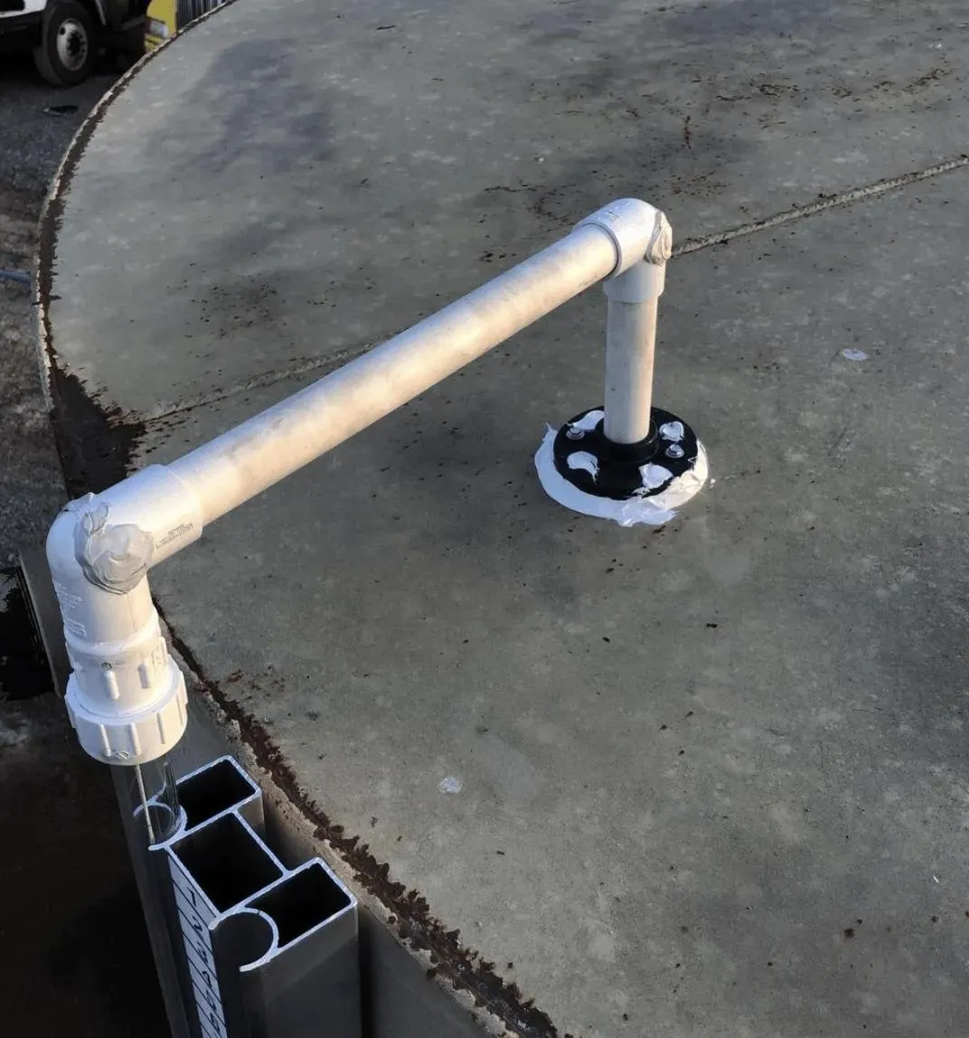 A close-up of a white PVC pipe setup on the top of a storage tank, demonstrating sealed plumbing to prevent vapor loss. This design enhances efficiency for industries using mechanical tank float level gauges.