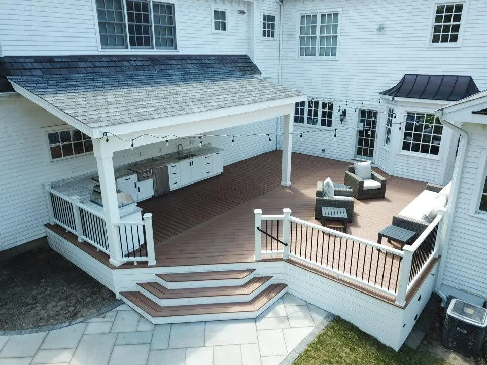 Covered composite deck with a shingled roof, outdoor kitchen, string lights and white railings on a white home in Wilmington, DE