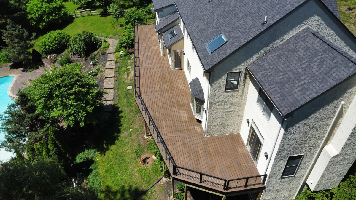 Aerial view of a long wraparound composite deck with cable railings beside a pool and garden in Wilmington, DE
