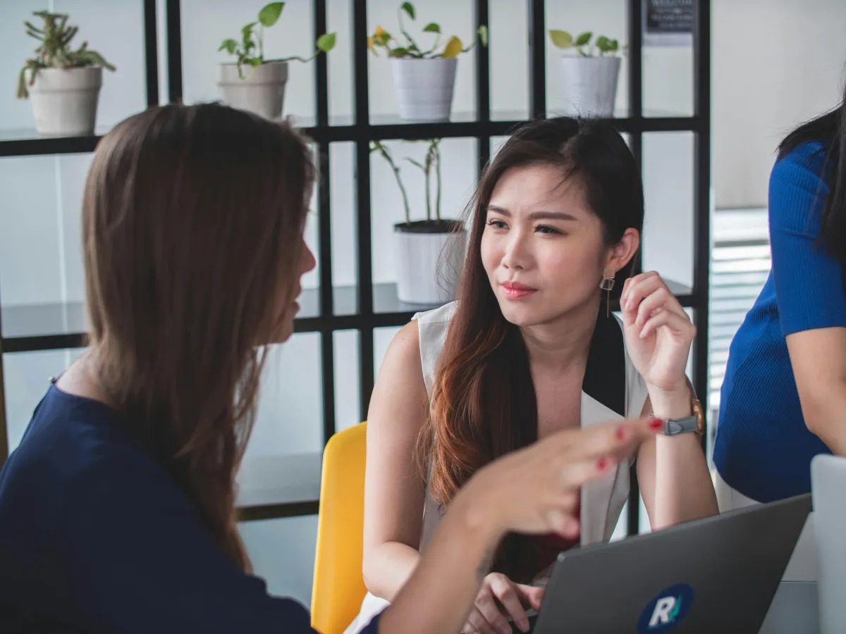 Two women talking while working on laptops