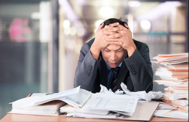 Stressed middle manager surrounded by paperwork and digital notifications in a modern office setting.