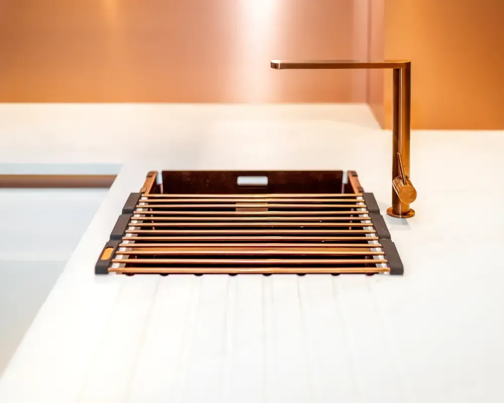 White kitchen countertop with copper undermount sink, integrated copper drying rack, and matching geometric copper tap by Blueprint Kitchens