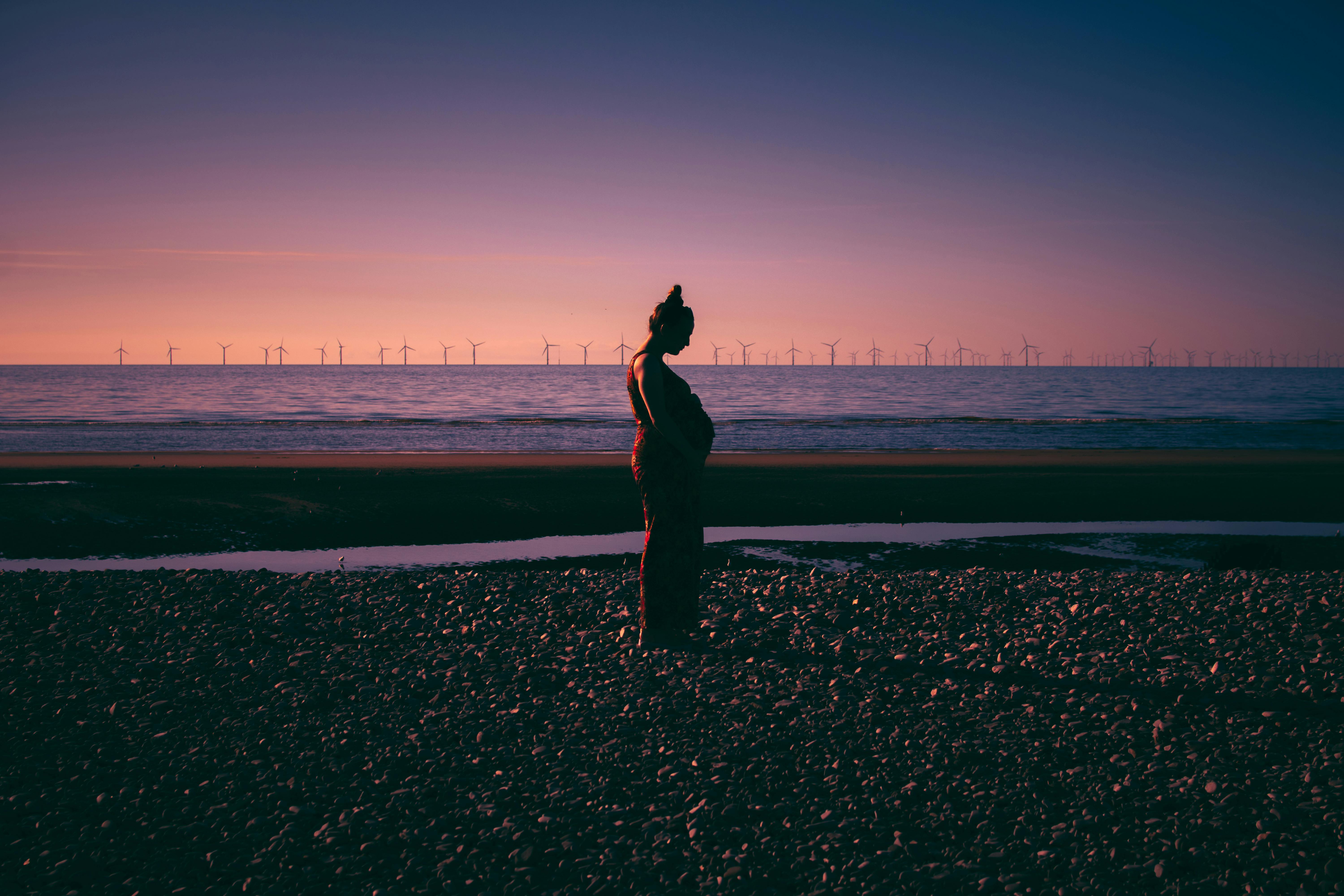 pregnant woman walking on a beach at sunset