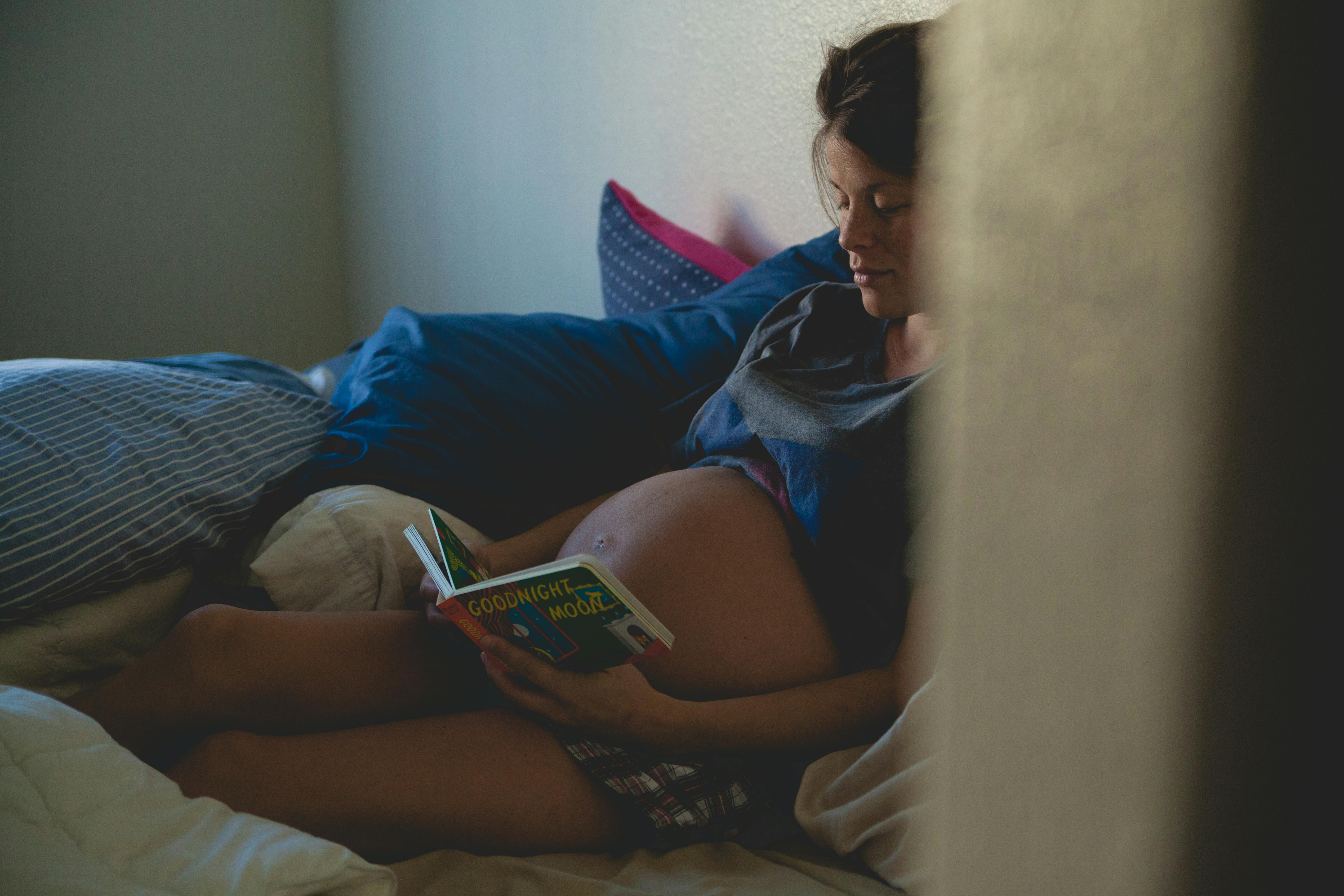 pregnant woman lying in bed reading a book