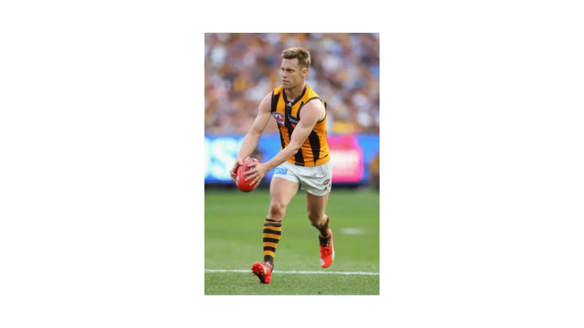 Young male AFL player with football in his hands about to kick. He is wearing white shorts, yellow and black shirt and socks with football boots.