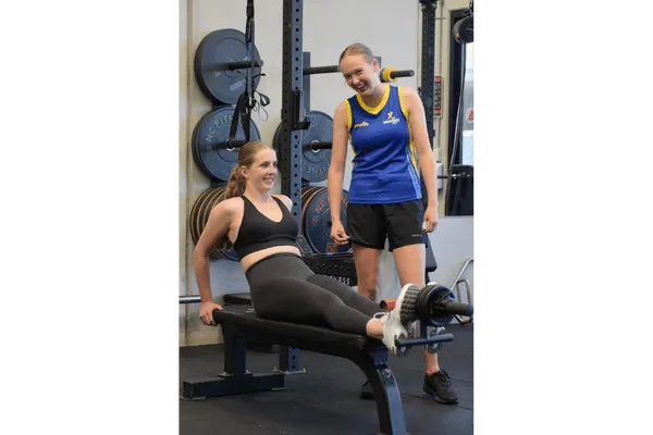 two female youth athletes undertaking strength training whilst one watches on