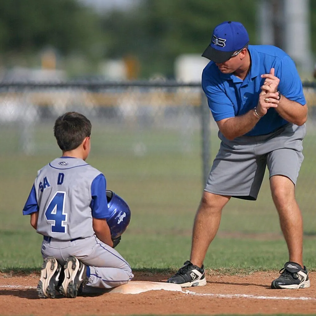 Male coach standing on pitch showing young autistic baseball player how to swing