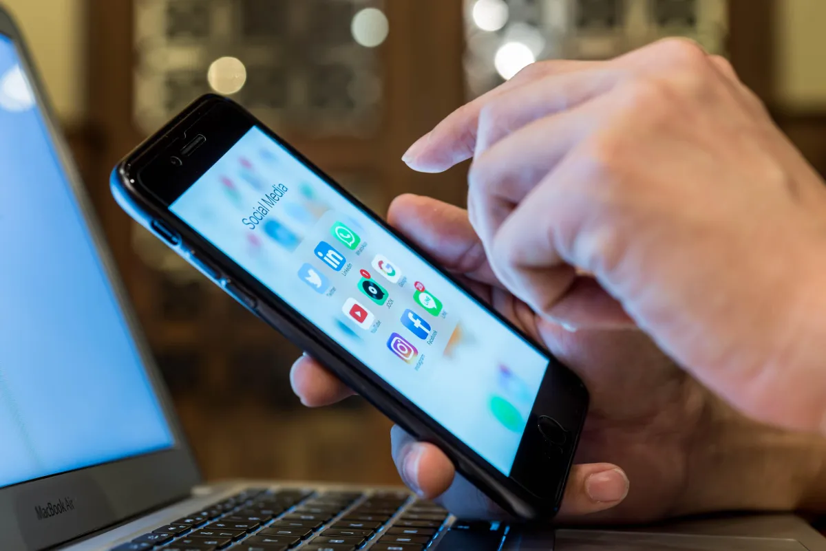  Person’s hand searching a phone screen with Social Media apps.