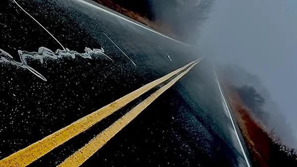 A moody, fog-covered road with yellow double lines stretching into the distance, symbolizing a journey or strategic direction. The scene evokes a sense of momentum, uncertainty, and forward movement.