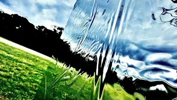 A distorted, abstract reflection of a grassy field and sky on a rippled, mirrored surface—symbolizing perspective, clarity, and transformation through a new lens.