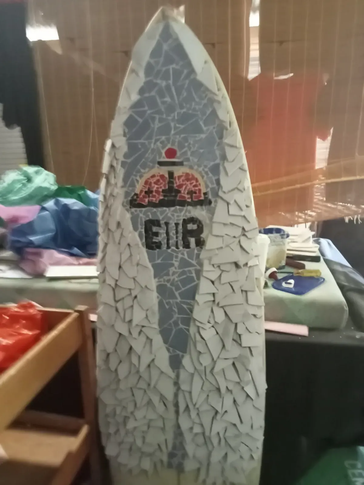 Work-in-progress mosaic surfboard featuring the EIR logo in the workshop