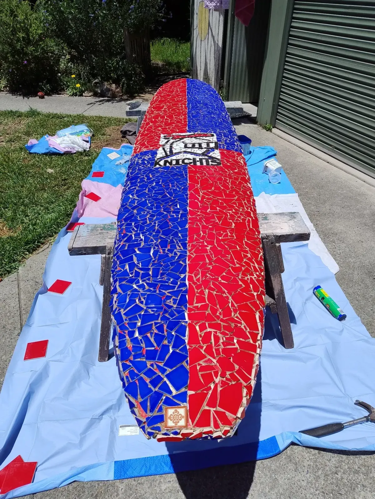 Red-and-blue mosaic surfboard letterbox featuring a Newcastle Knights logo during workshop finishing