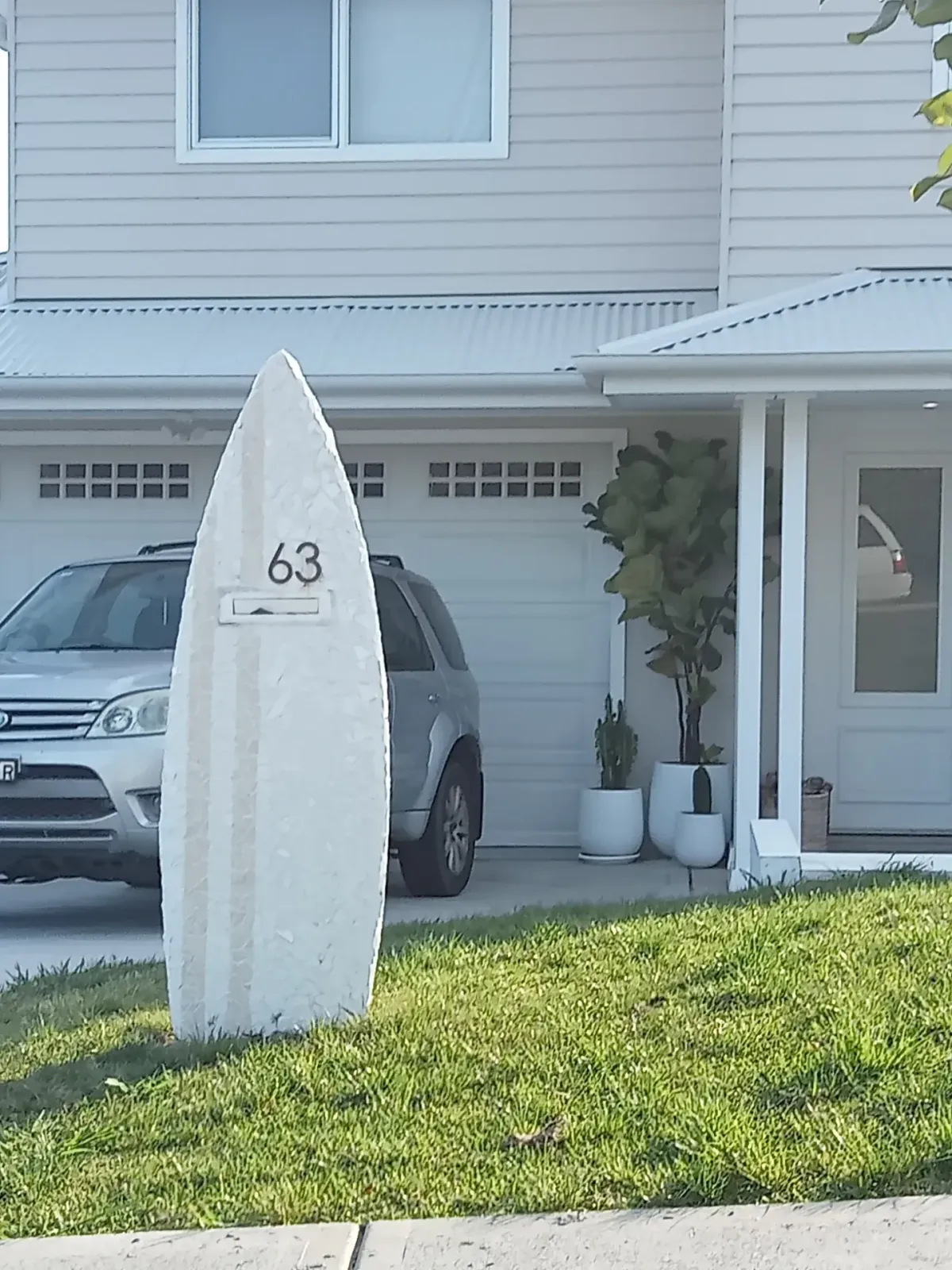 All-white mosaic surfboard letterbox with house number 63 in a modern coastal driveway