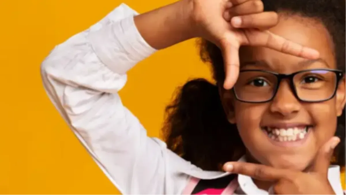 Young Black child in front of a yellow background using their thumbs and index fingers to frame their face.
