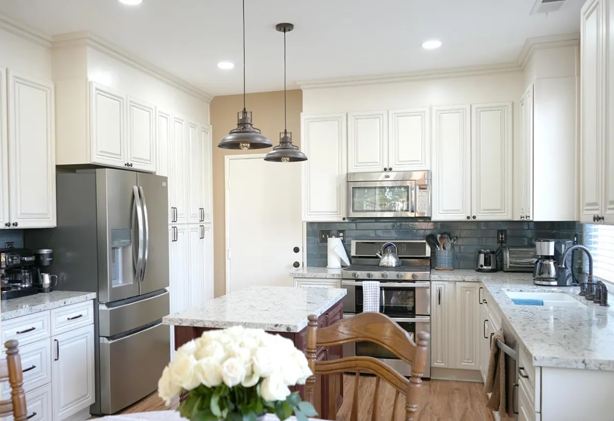 Modern kitchen with white cabinetry, stainless steel refrigerator, granite countertops, pendant lights, and a dark subway tile backsplash.