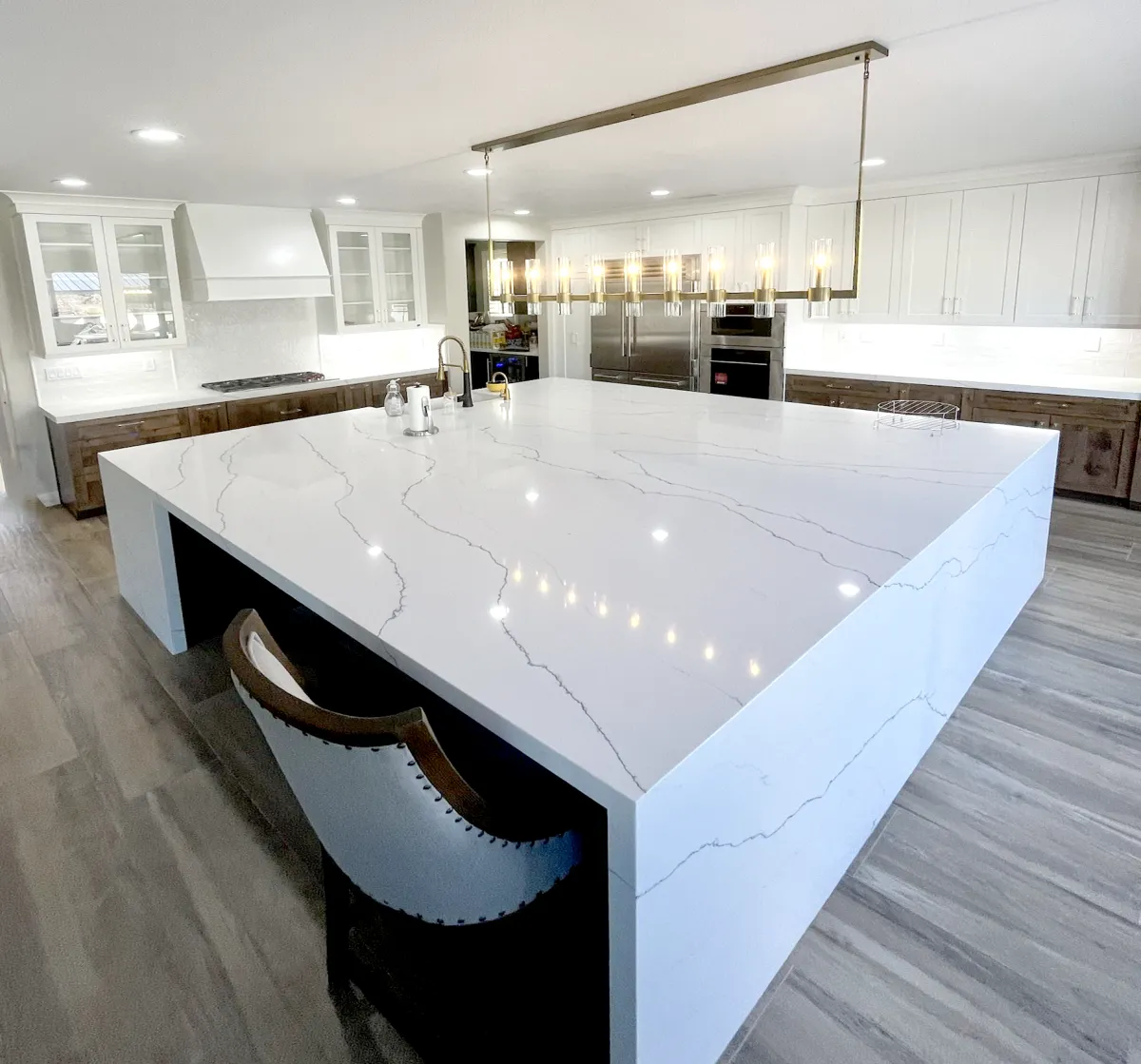 Modern kitchen with a large waterfall quartz island, brass pendant lighting, white cabinetry, and stainless steel appliances.