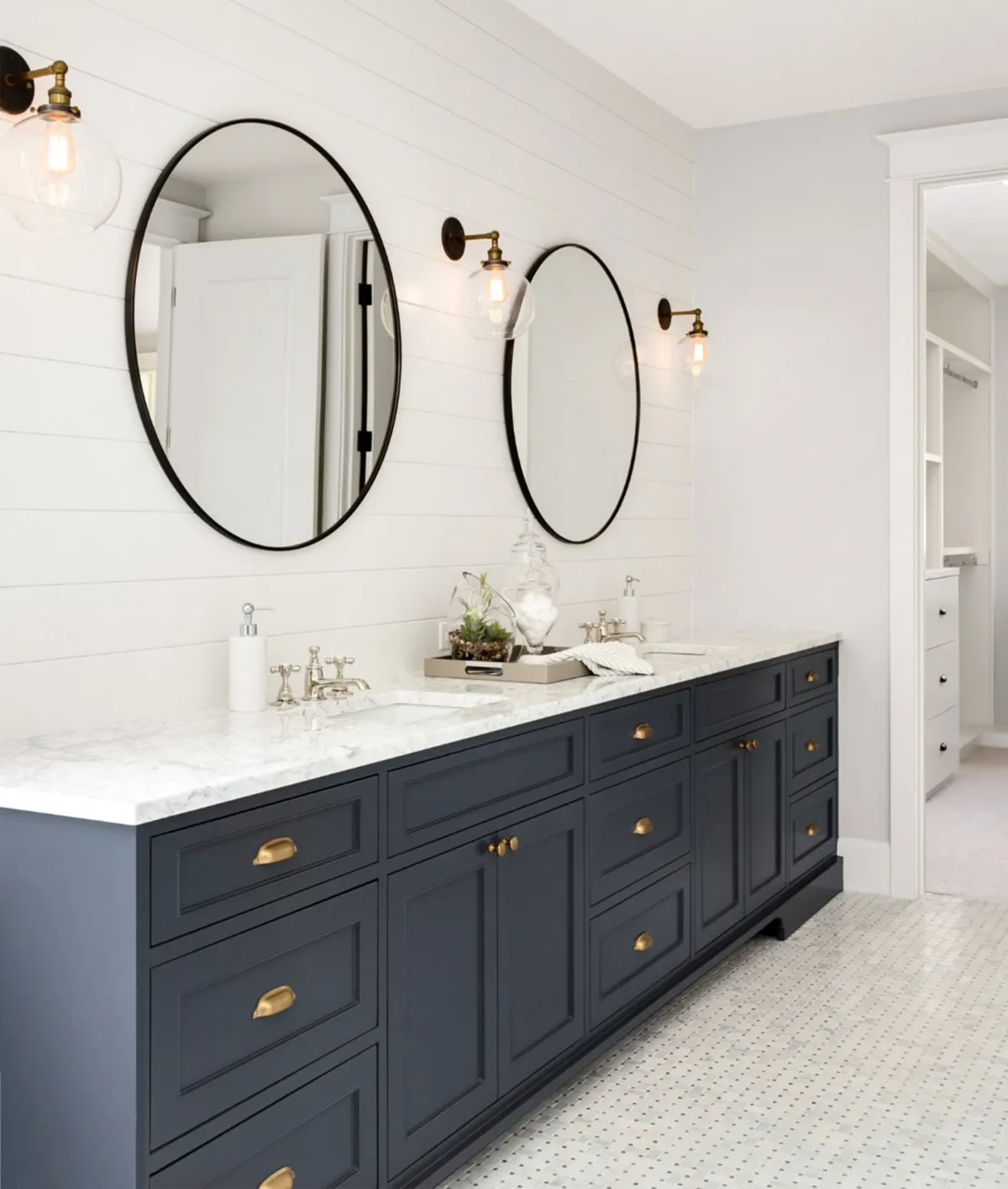 Elegant bathroom with a navy double vanity, marble countertops, round black-framed mirrors, and brass hardware against shiplap walls.