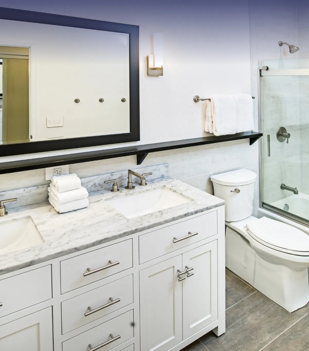 Modern bathroom with a white double vanity, marble countertop, large framed mirror, glass-enclosed shower, and chrome fixtures.