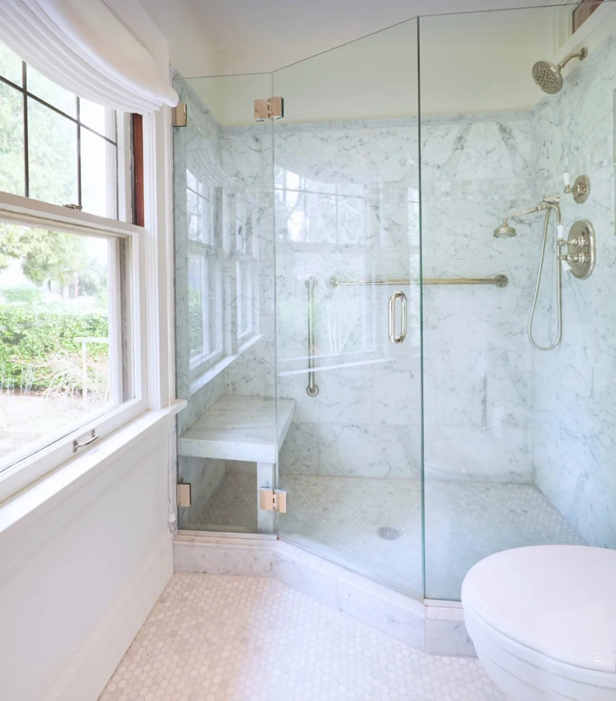 Elegant bathroom with a marble walk-in shower, built-in bench, chrome fixtures, and a large window with outdoor views.