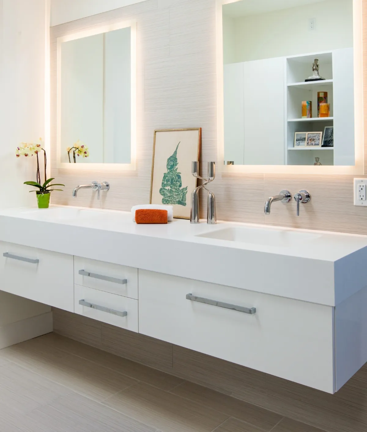 Modern bathroom with a floating double vanity, integrated sinks, backlit mirrors, minimalist chrome fixtures, and decorative accents.