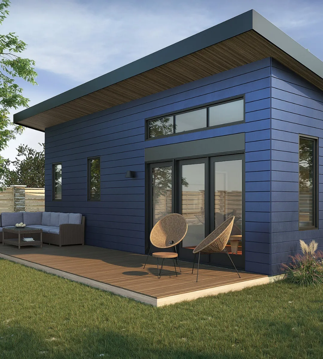 Modern ADU with blue siding, sloped roof, wooden deck, and outdoor seating surrounded by a landscaped yard.