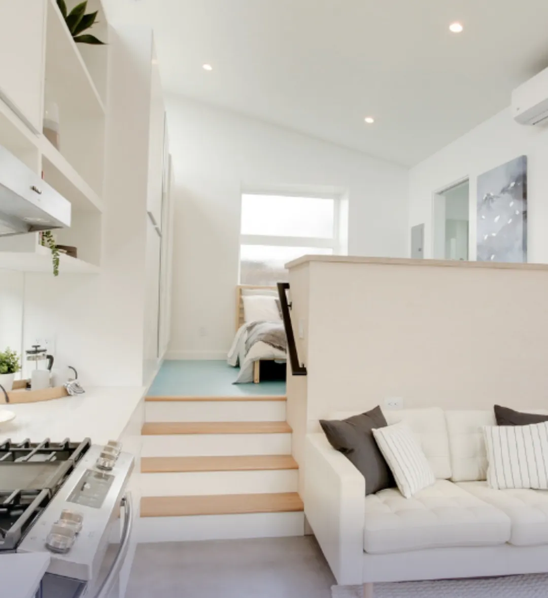 Bright ADU interior with an elevated bedroom, white kitchen cabinetry, and an open living area in a modern minimalist design.
