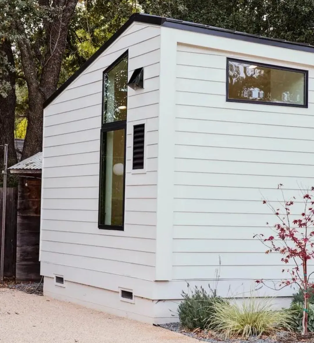 Compact ADU with white siding, black-framed windows, and a modern minimalist design surrounded by greenery.
