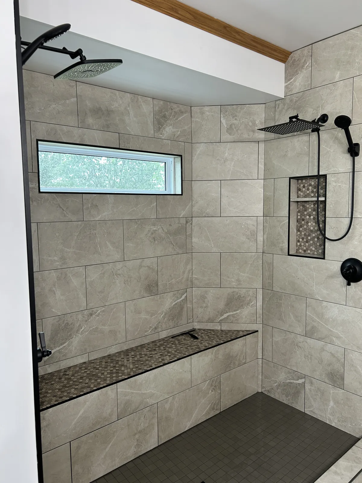 Finished tile shower with bench and black fixtures in a primary bathroom remodel by Archstone Homes