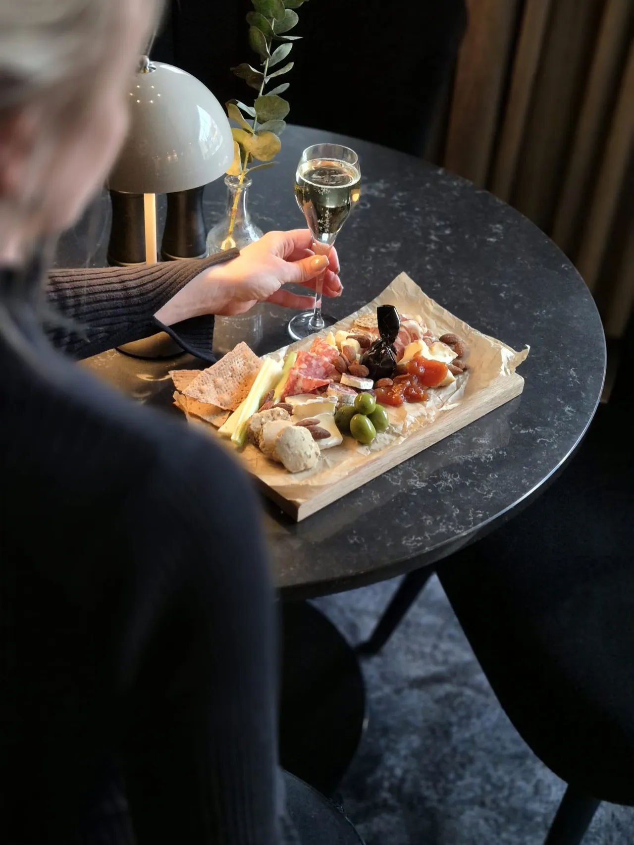En charkbricka med oliver, ost och mandlar och ett glas bubbel på ett runt stenbord