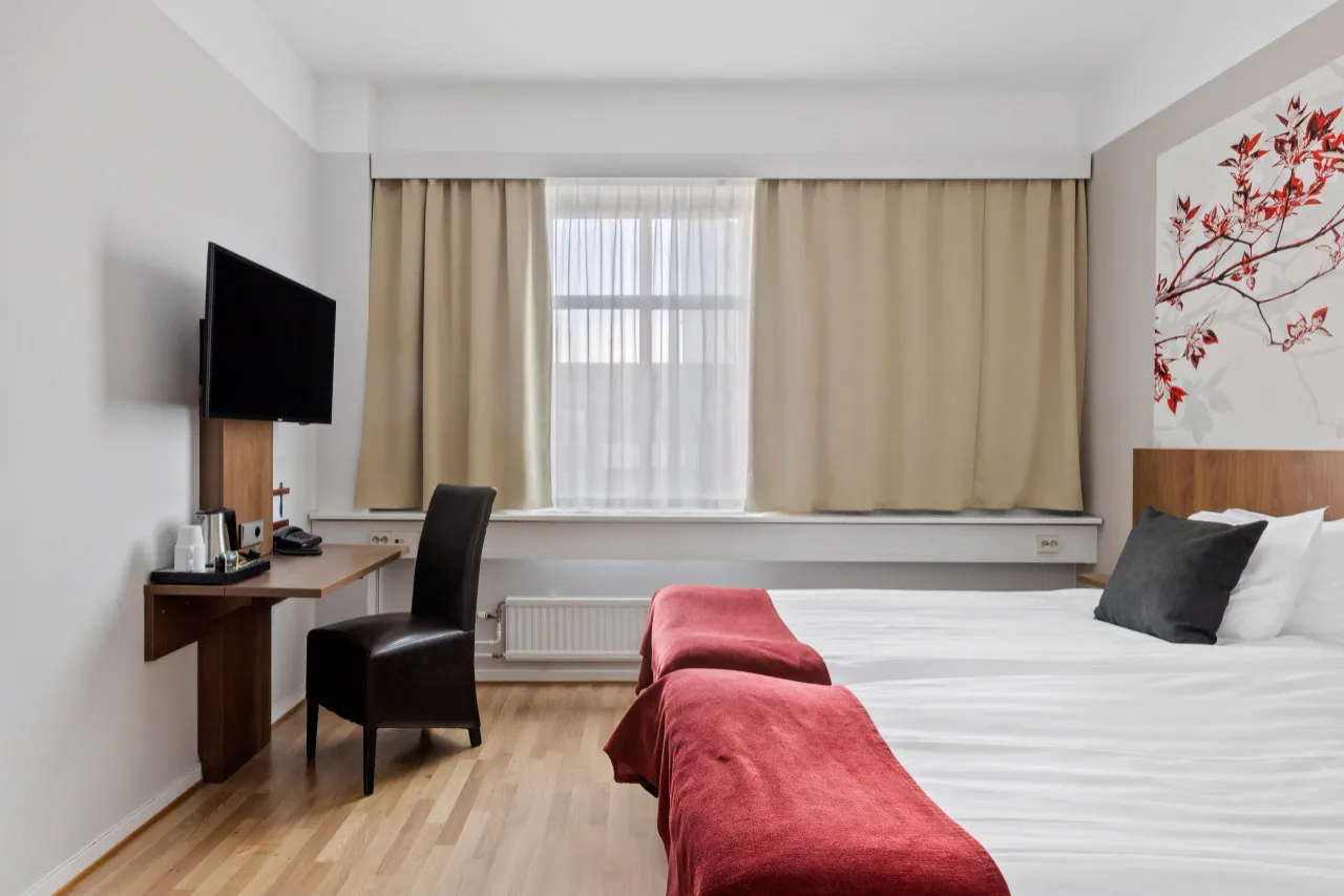 Dubbelrum med två sängar och röda överkast, skrivbord och tv på väggen