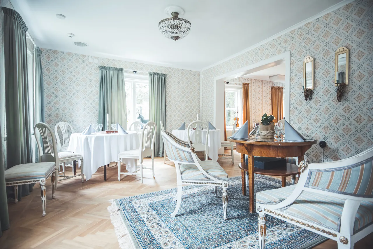 Salong med vita stolar, dukade bord och blommiga tapeter