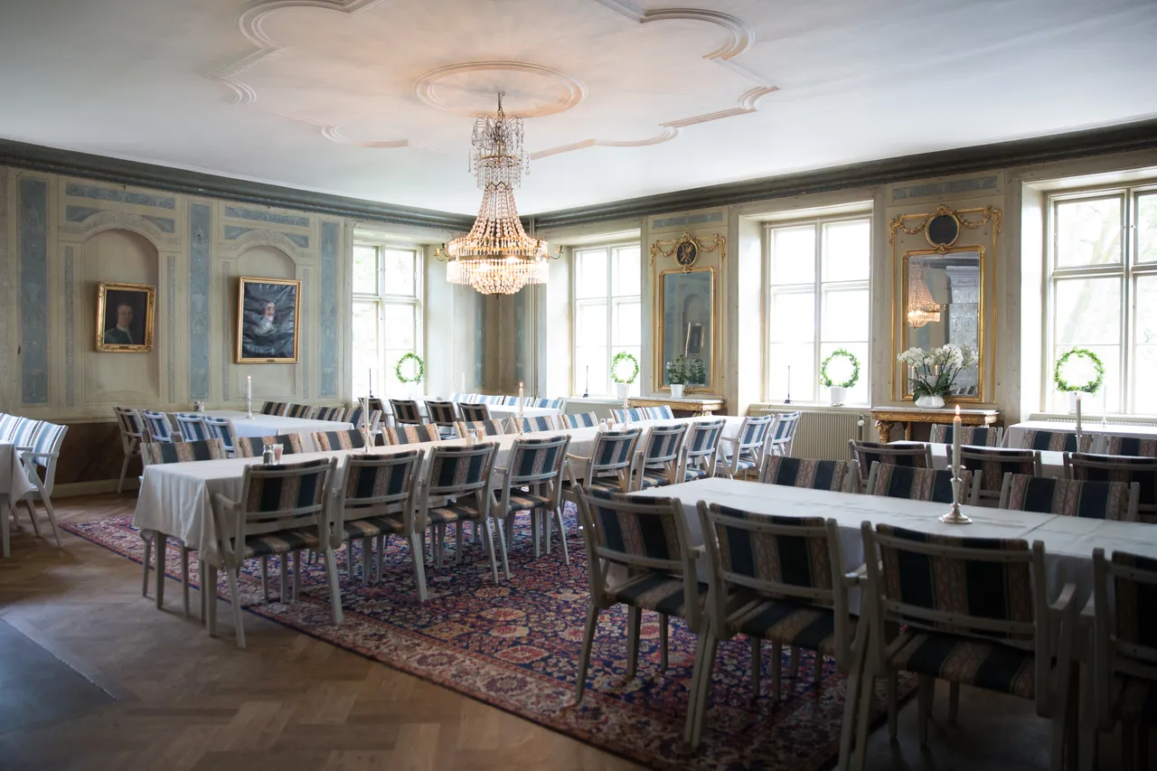 Festvåningen med dukade långbord, randiga stolar och en kristallkrona i taket