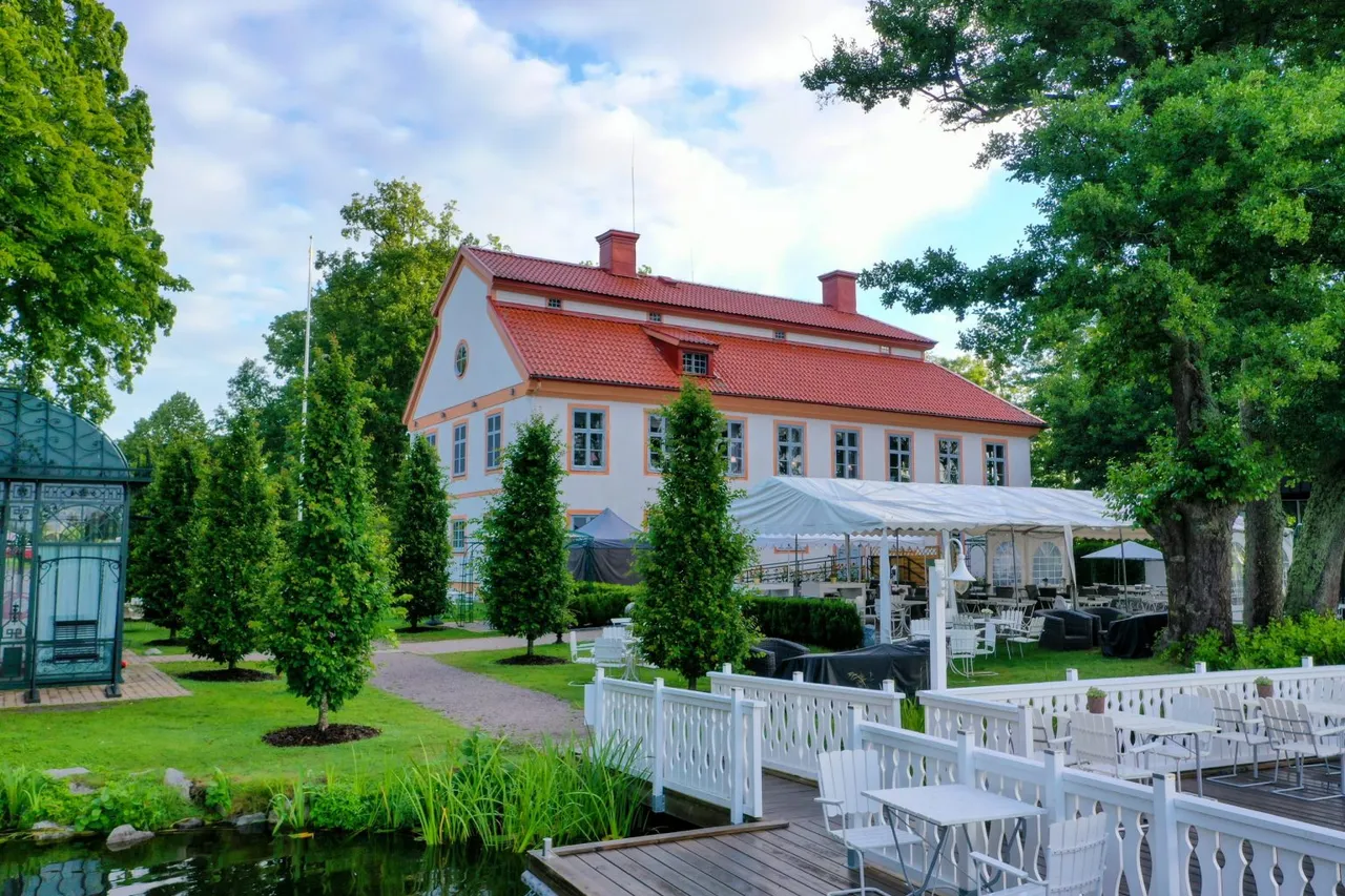 Herrgården och uteserveringen med vita trästaket och bryggan vid sjön en sommardag