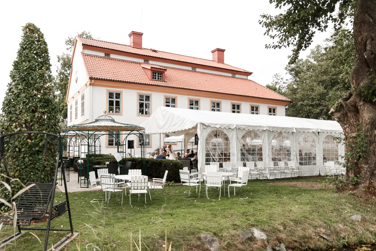 Sommarfest på gräsmattan intill herrgården, med ett vitt tält, trädgårdsmöbler och en lövad paviljong