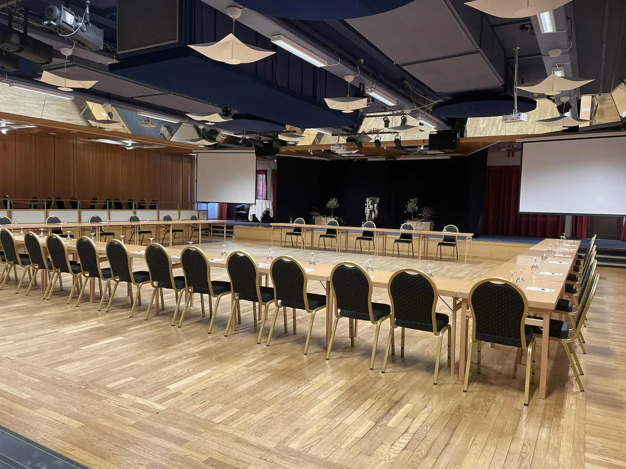Den stora salen möblerad med långa bord i U-form framför scenen och två projektordukar