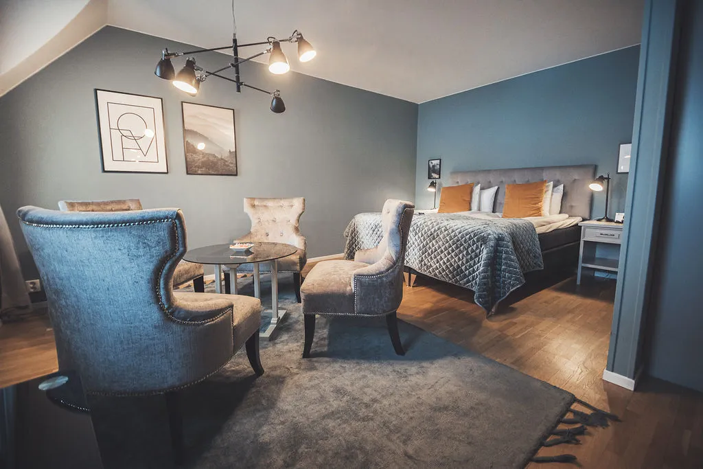 Hotellrum med blågrå väggar, sammetsfåtöljer och dubbelsäng i varmt lampljus