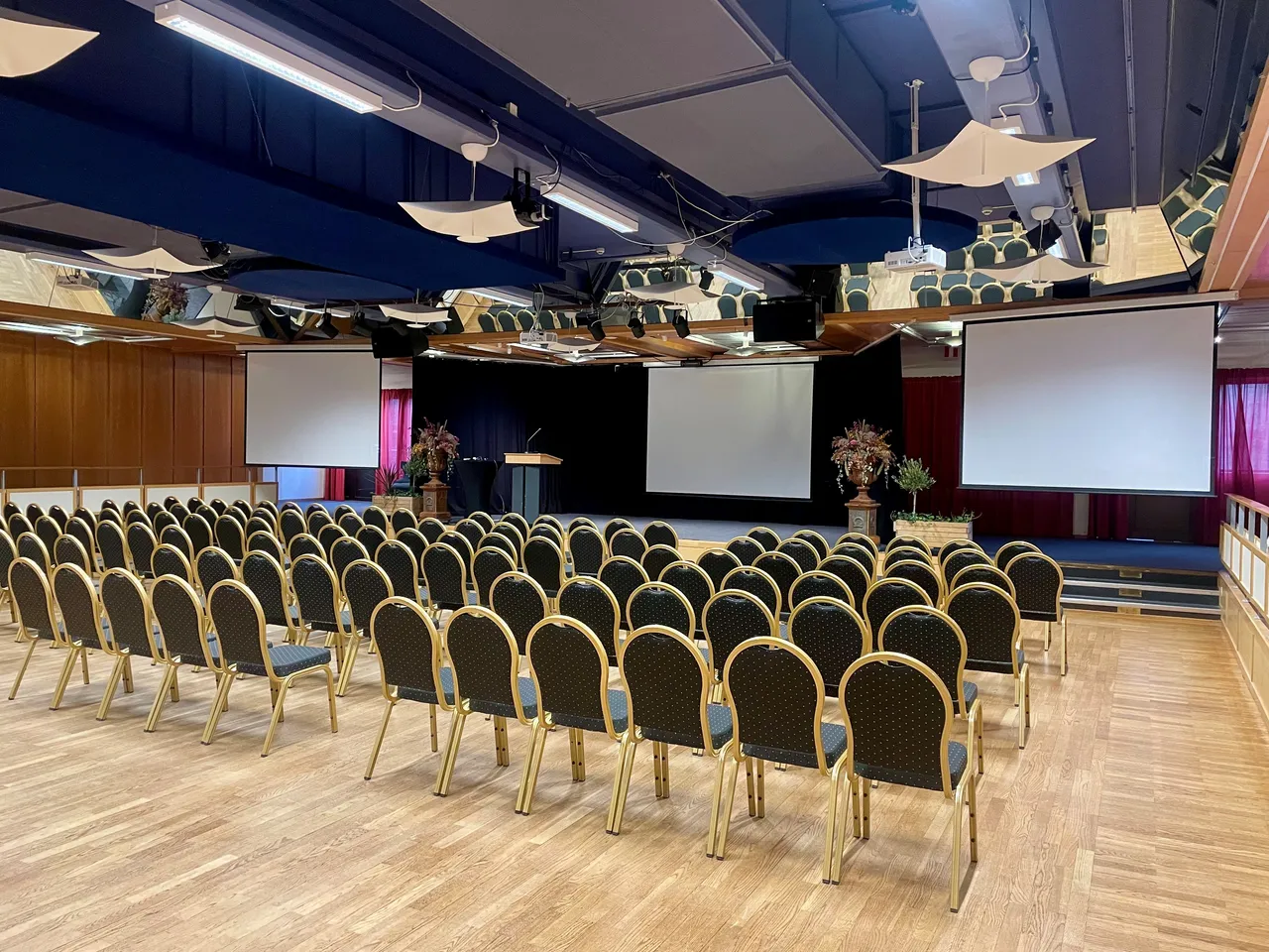 Den stora salen möblerad i biosittning med tre projektordukar och en talarstol på scenen