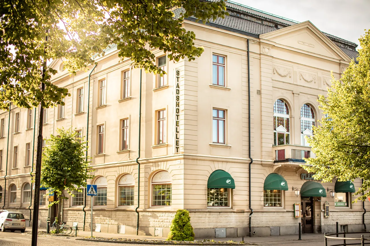 Hotellets ljusa fasad i kvällssol, inramad av lummiga träd