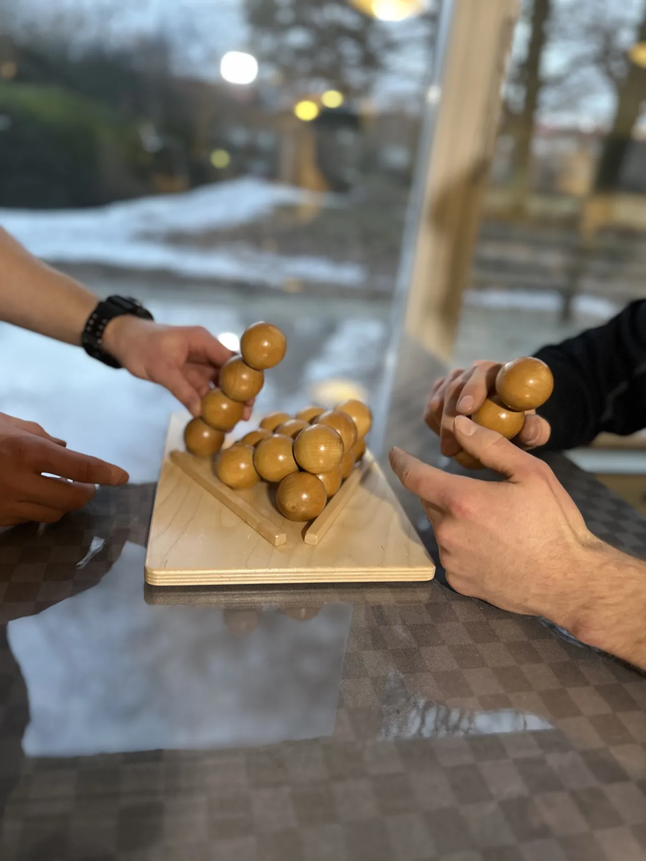 Händer som löser ett klurigt träpussel med kulor på ett bord
