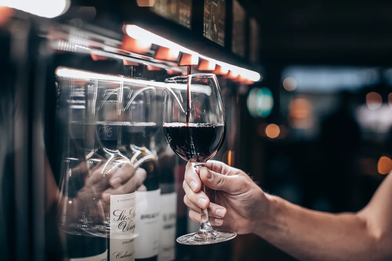 Ett glas fylls med rött vin ur en vinautomat med upplysta flaskor