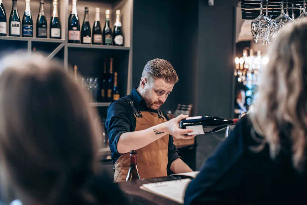 Bartender i förkläde häller upp rött vin för gäster vid baren i vinbaren