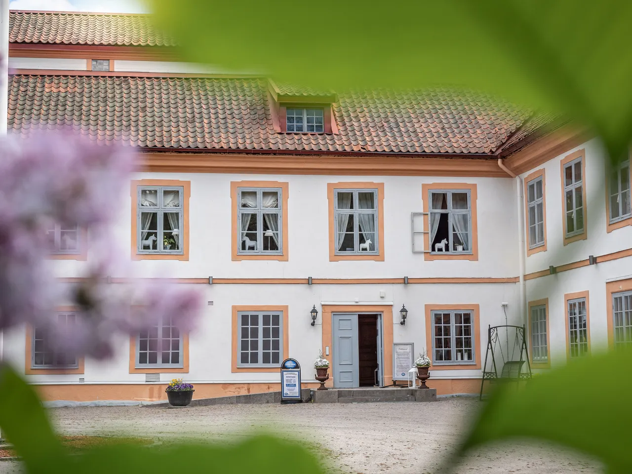 Herrgårdens ljusa fasad med entrén, sedd genom blommande syren
