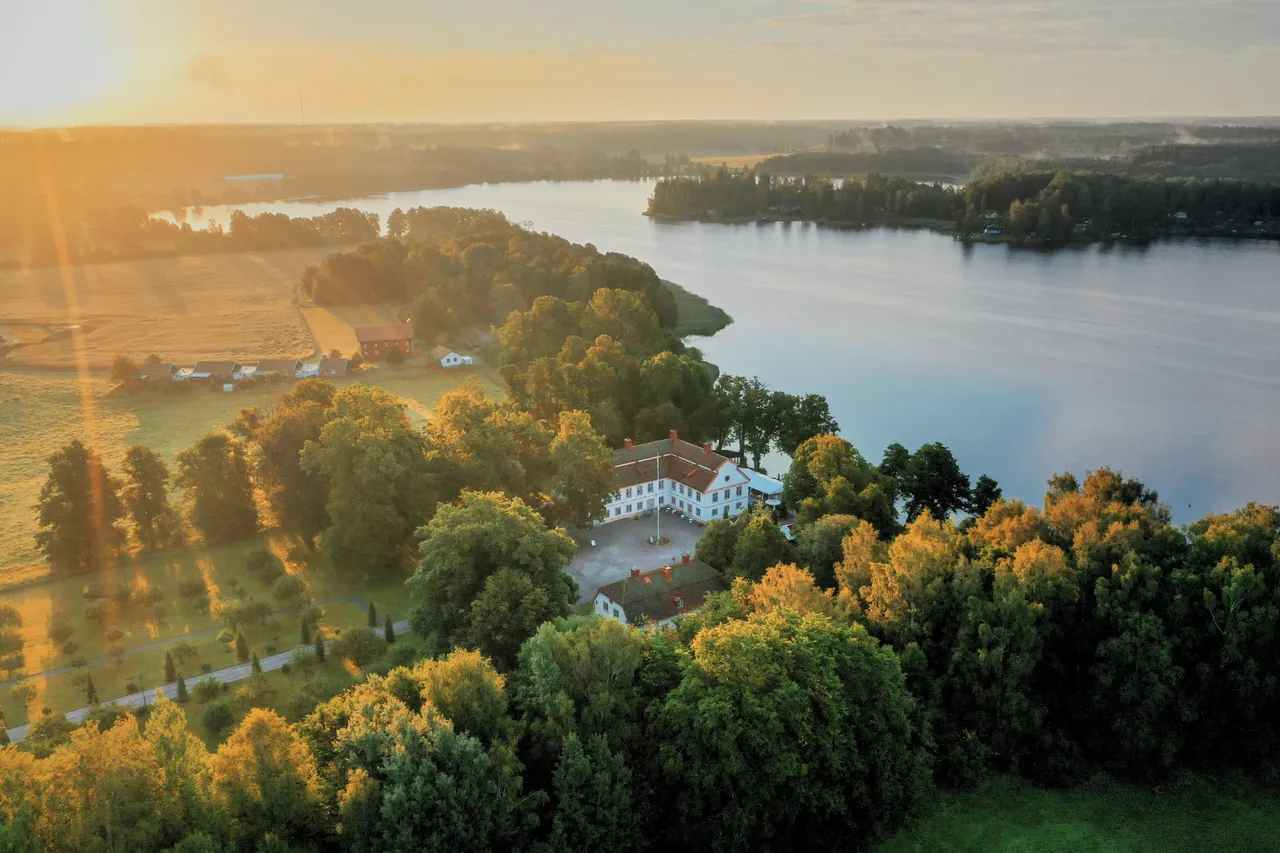 Herrgården bland lummiga träd vid sjön, sedd från ovan i lågt solljus