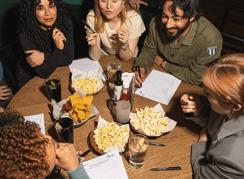 Ett kompisgäng med popcorn och quizpapper runt ett bord på O'Learys