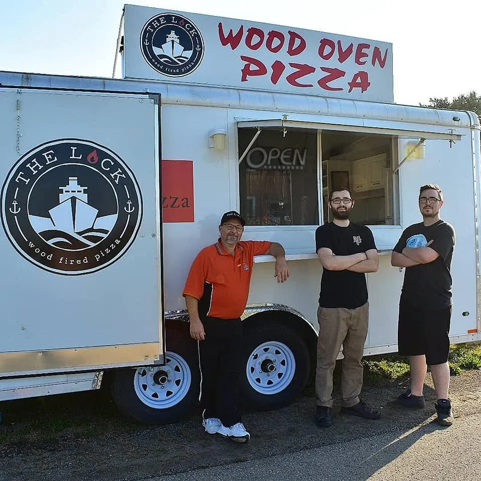 The Lock's mobile wood oven pizza trailer with three team members in front