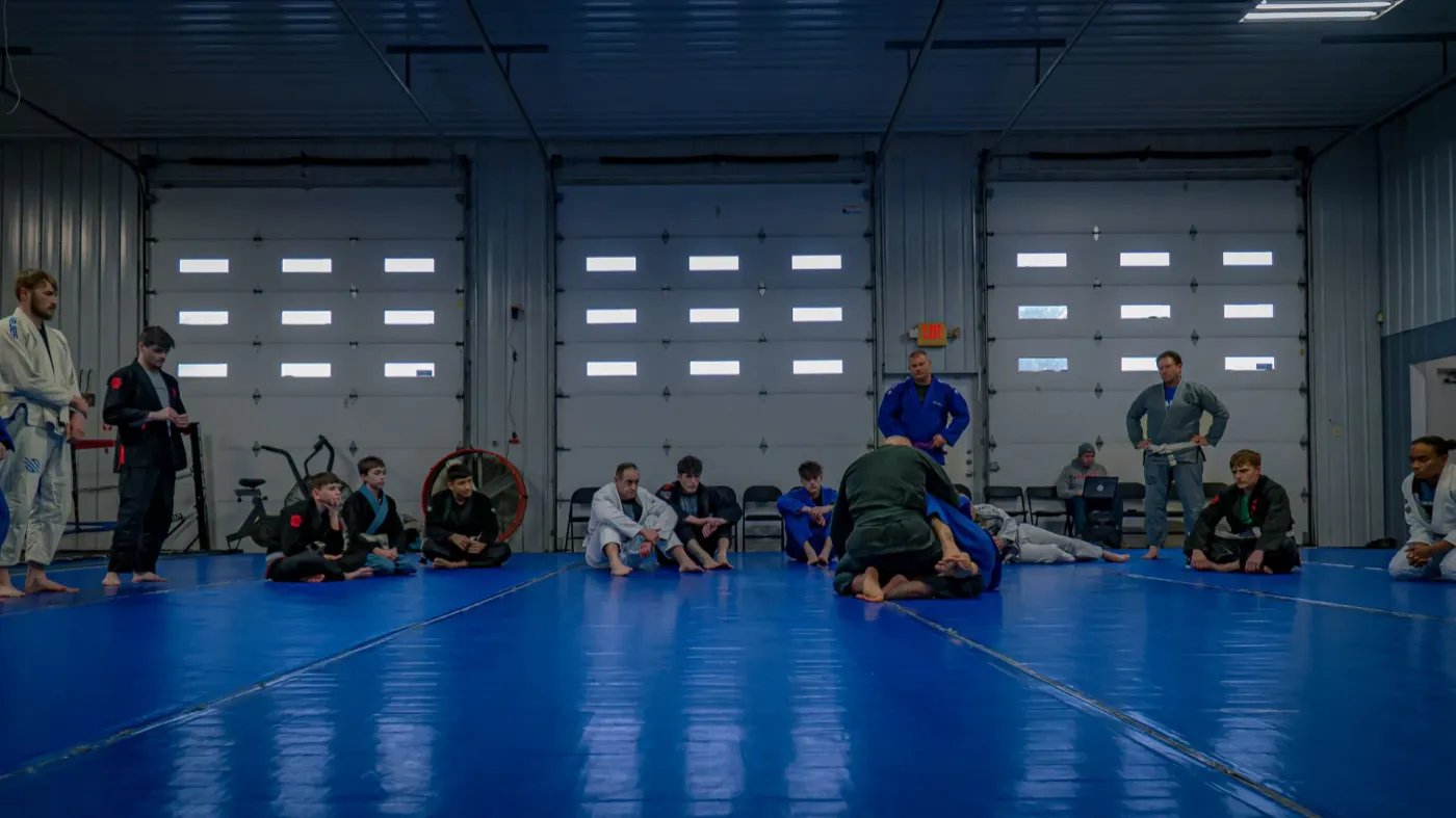 The open training floor at Delta Grappling Academy with students rolling on blue mats