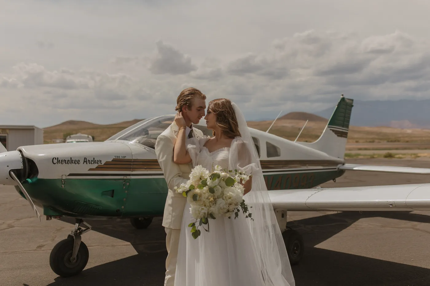 Bride and groom embracing beside a vintage airplane with wedding florals by Flamingo Friday Floral Co.